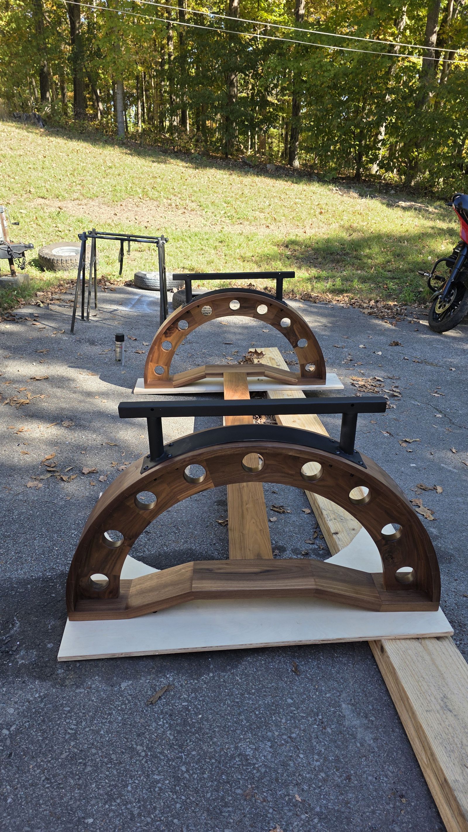 Two walnut arch bases with black steel top brackets lined up on a driveway during the build