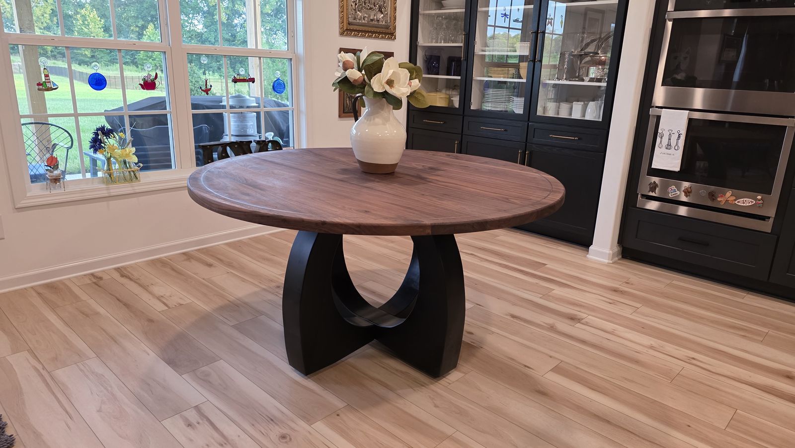 60-inch round walnut dining table with black arch base, installed in a client's kitchen